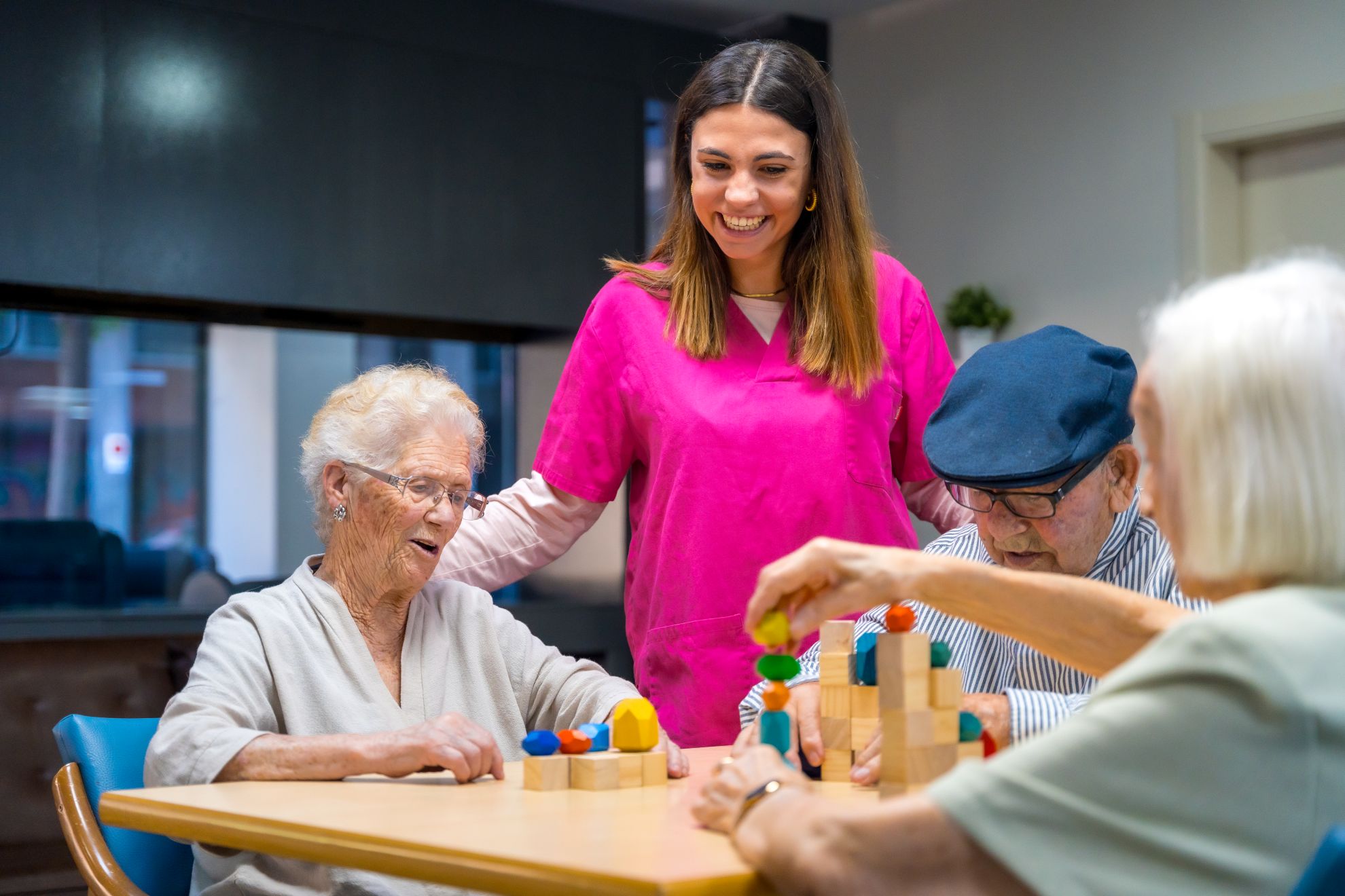 Smiling nurse engaging elderly residents in a skill-building activity with colorful blocks